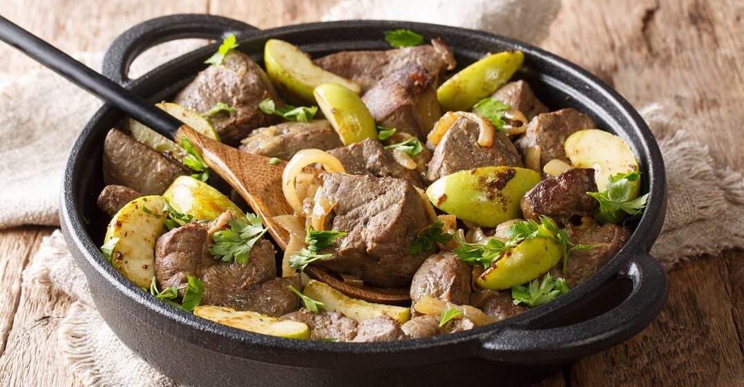 best food in Berlin: roasted beef liver with green apples, onions and herbs close-up in a pan on the table