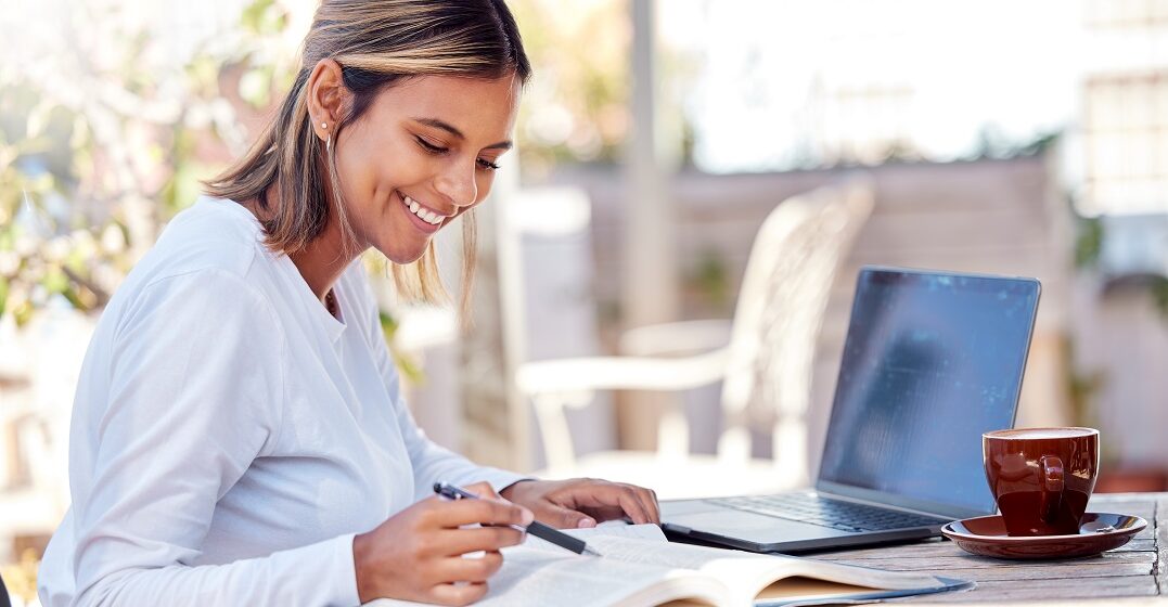 Female student reading a book next to an open laptop learning about formal vs. informal Spanish
