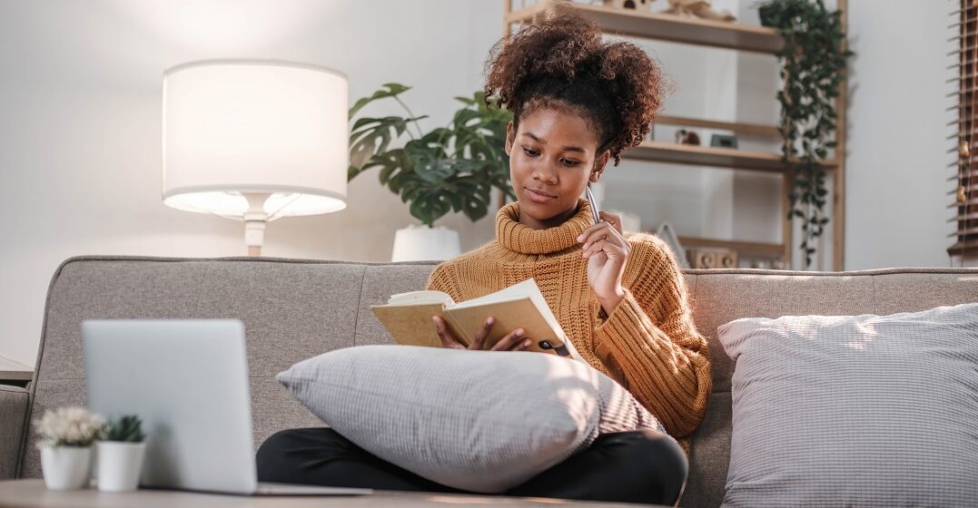 Junge Frau auf ihrem Sofa sitzt am Laptop und lernt den Imperativ auf Deutsch