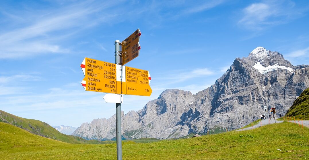 Gelbes Schild mit lustigen Ortsnamen der Schweiz vor Bergpanorama