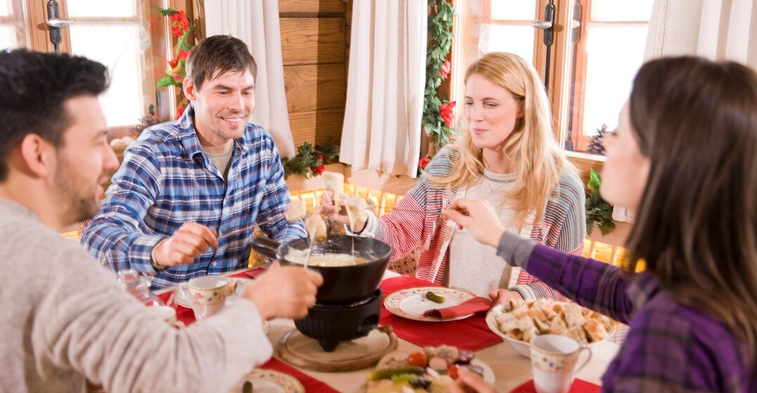 Freunde sitzen an einem Tisch und essen Fondue- ein typisches Schweizer Gericht