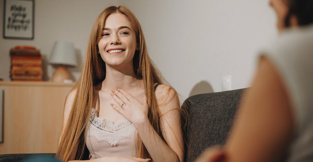 Young woman sitting and pointing at herself to explain soy vs. estoy in Spanish