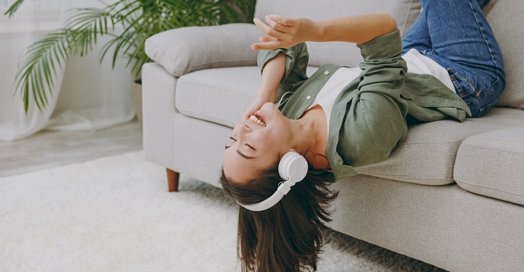 Woman laying on a couch upside down listening to a business English podcast with headphones on