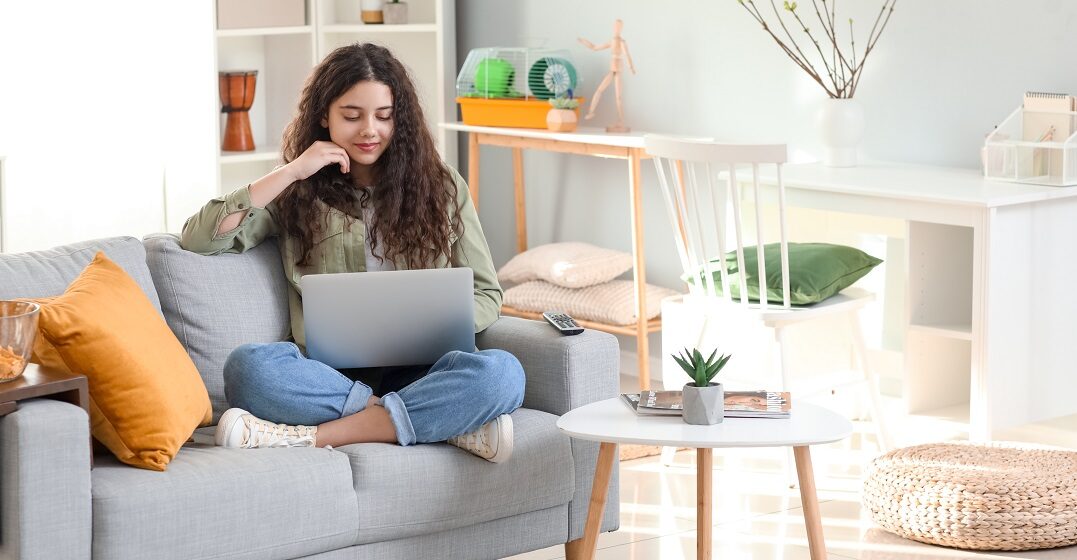 Young woman using her laptop sitting on a couch studying the personal pronouns in English