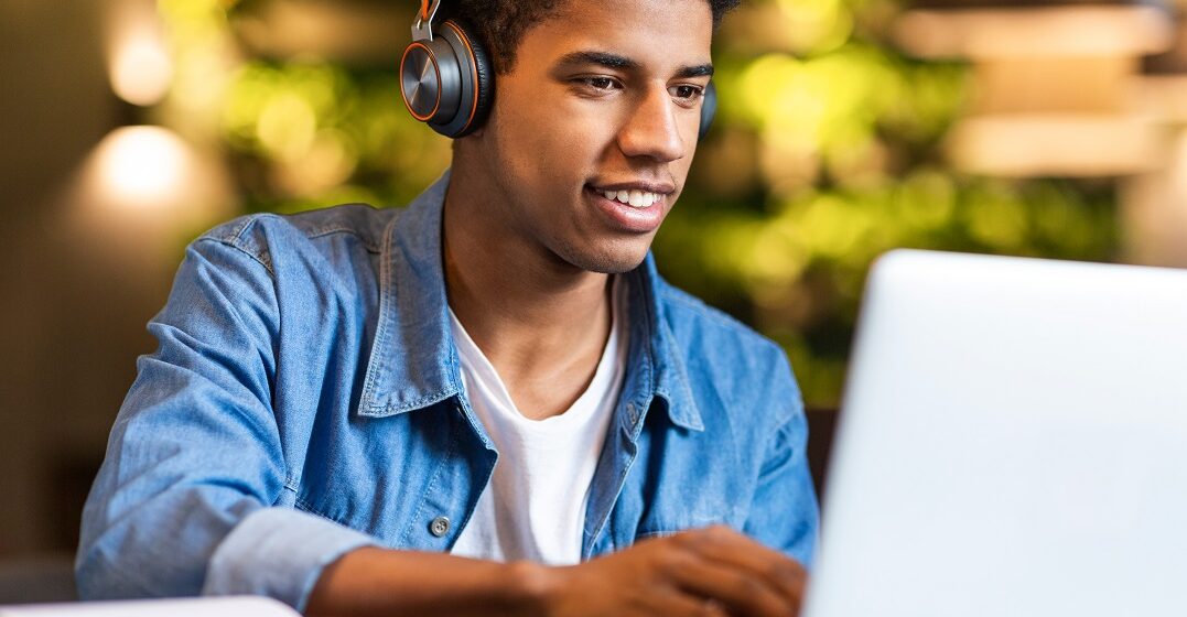 hombre afroamericano, sonriendo al portátil mientras aprende el pasado continuo en inglés