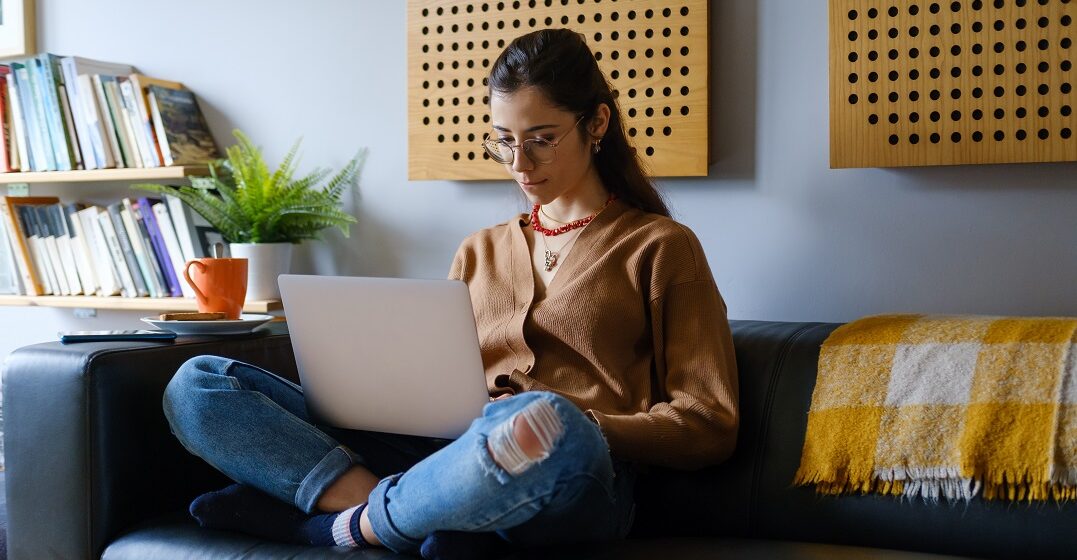 Woman sitting on a couch with her laptop studying the use of se in Spanish