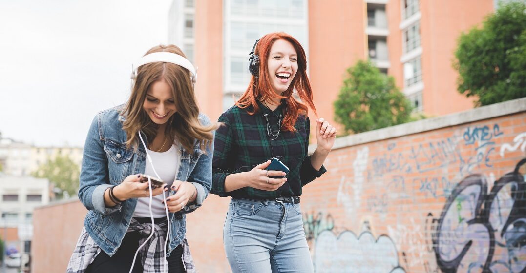 Two young women on a street with headphones listening to popular Swiss songs