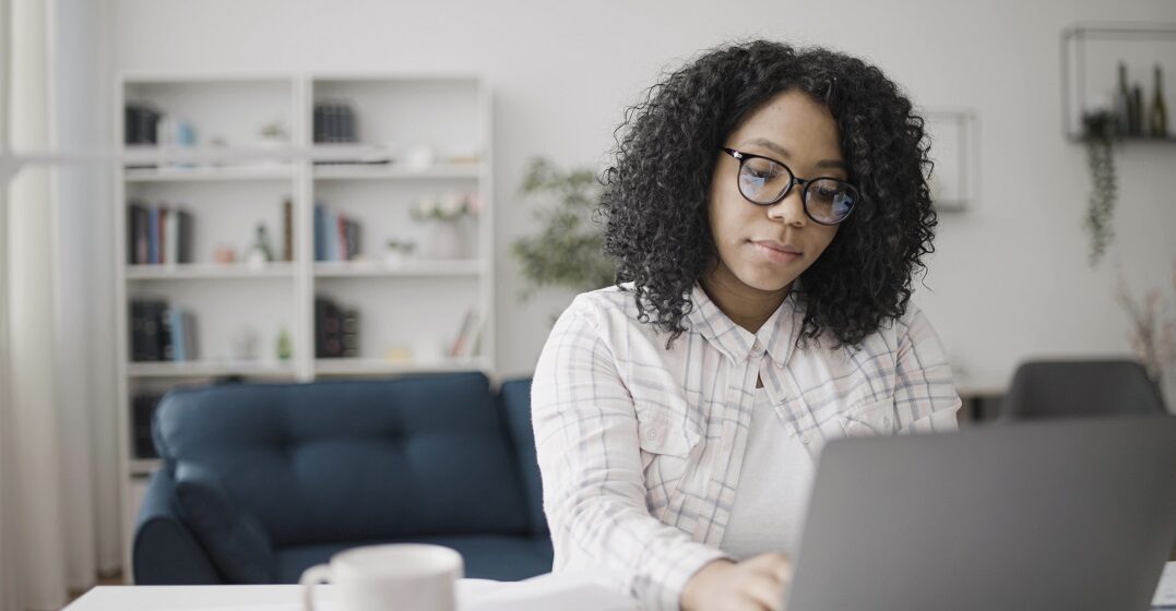 Eine junge Afrokamerikanerin sitzt am Laptop und lernt die Modalverben auf Deutsch
