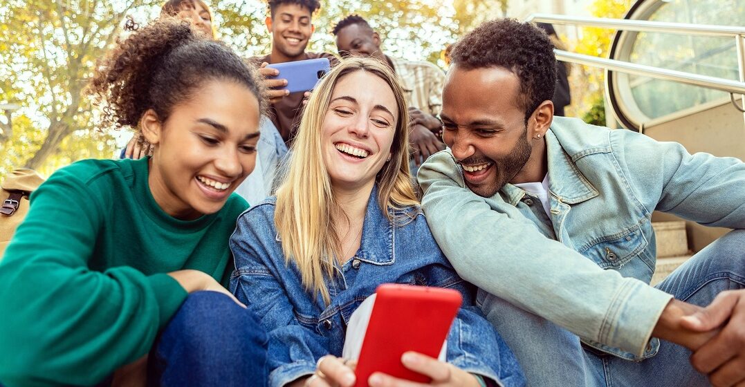 Three friends looking at a smartphone laughing about aggressive German words