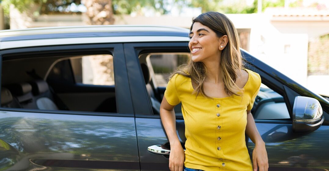 Young smiling woman standing next to her car learning the car parts in English