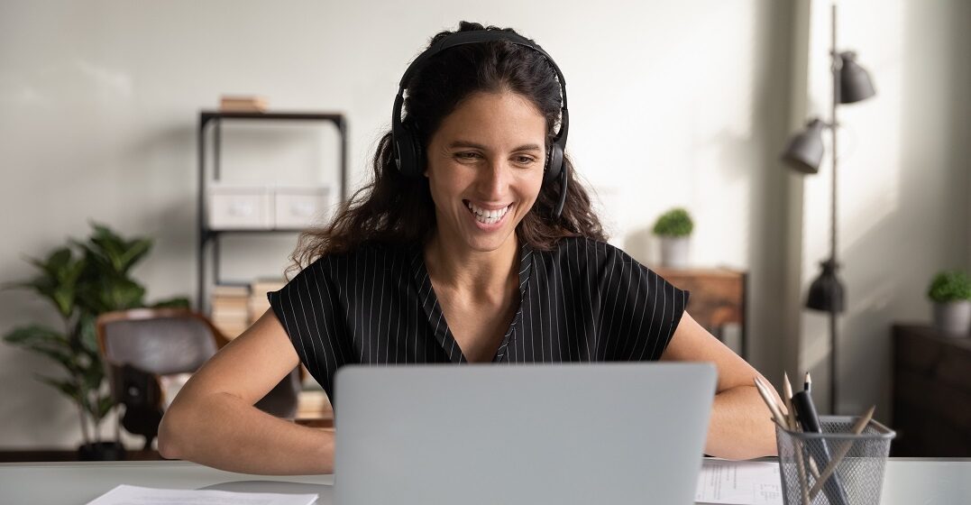 Eine lachende Frau sitzt vor ihrem Laptop und übt für ihre Deutschprüfung