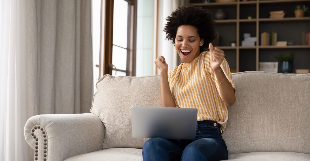 YOung woman sitting on a couch with her laptop making the German gestures of pressing her thumbs