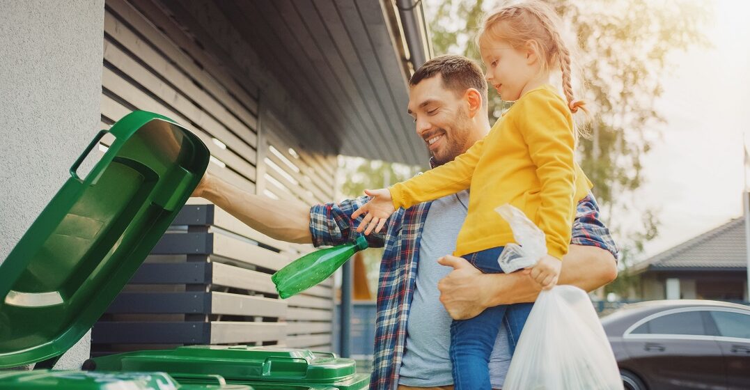 Ein Vater steht mit seiner Tichter an einer Mülltonne und bringt ihr Recycling in der Schweiz bei