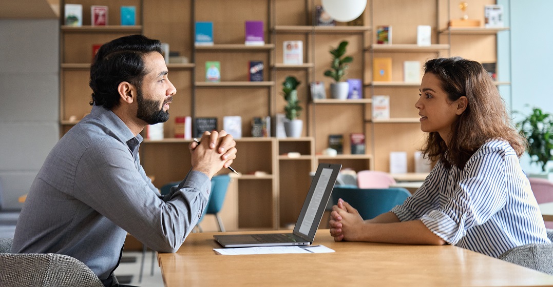 A man with a laptop sitting across a woman asking basic German questions