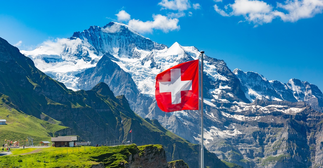 Swiss flag waving in front of a mountain range as a symbol of the most famous Swiss people