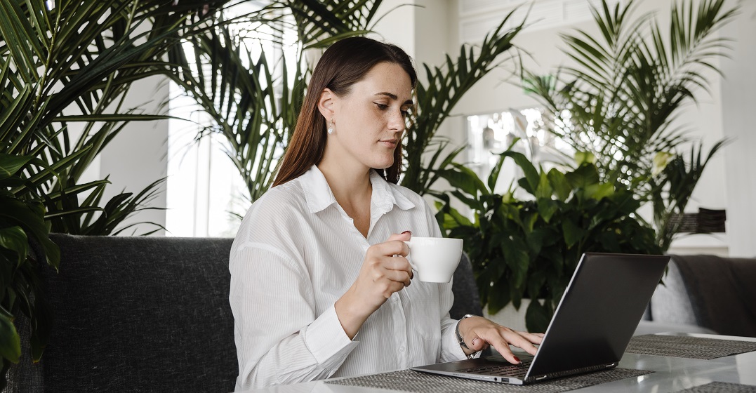 Young woman is drinking coffee at her laptop while learning one of the hardest languages for Spanish speakers