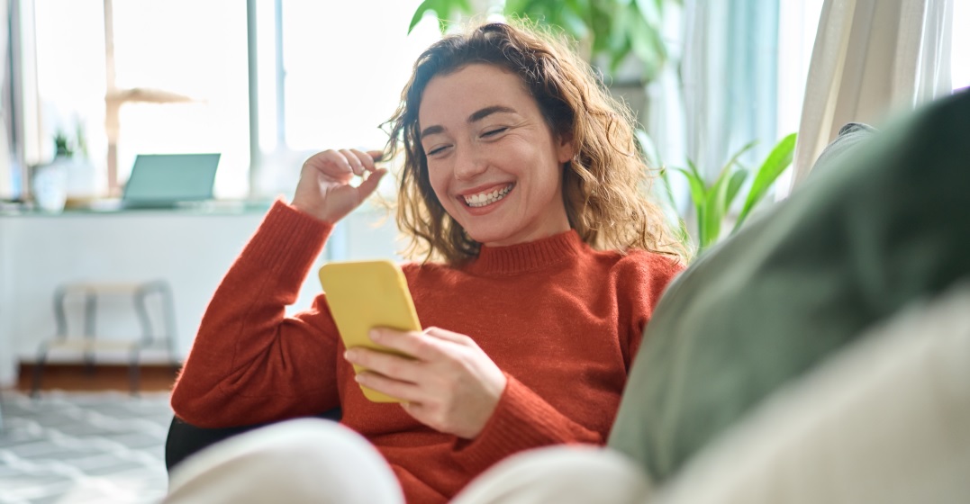 young woman sitting on a couch reading funny German last names on her phone