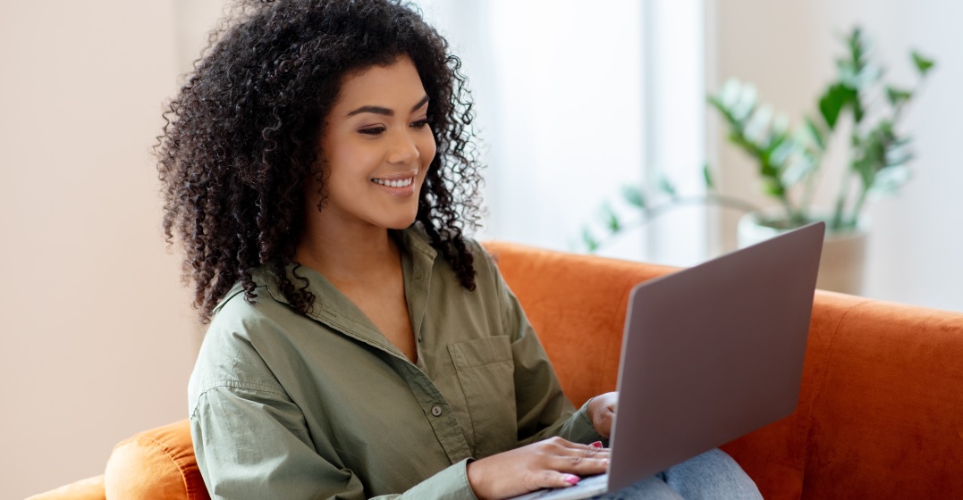 Smiling woman sits on the couch with her laptop studying the German conditonal sentences