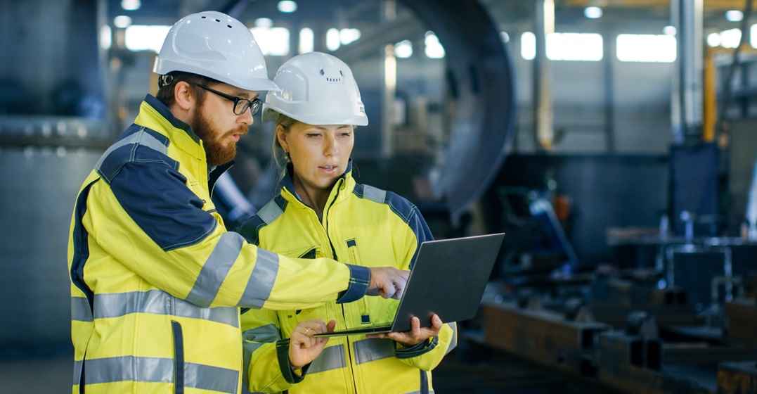 Male and female engineers wearing hemlemts looking at a laptop together - A popular German profession