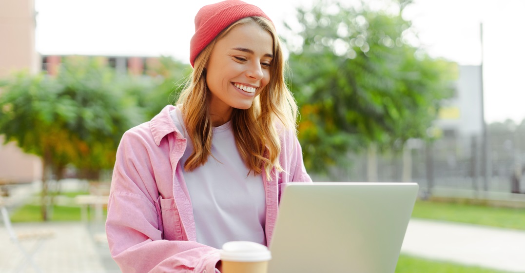 Smiling woman sits outside at her laptop learning the German subjunctive mode