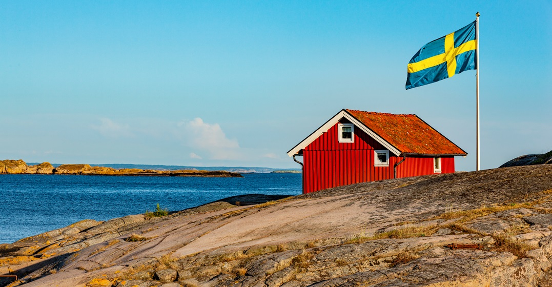 Red house in Sweden with a Swedish flag as a presentation of Swedish vs. German language