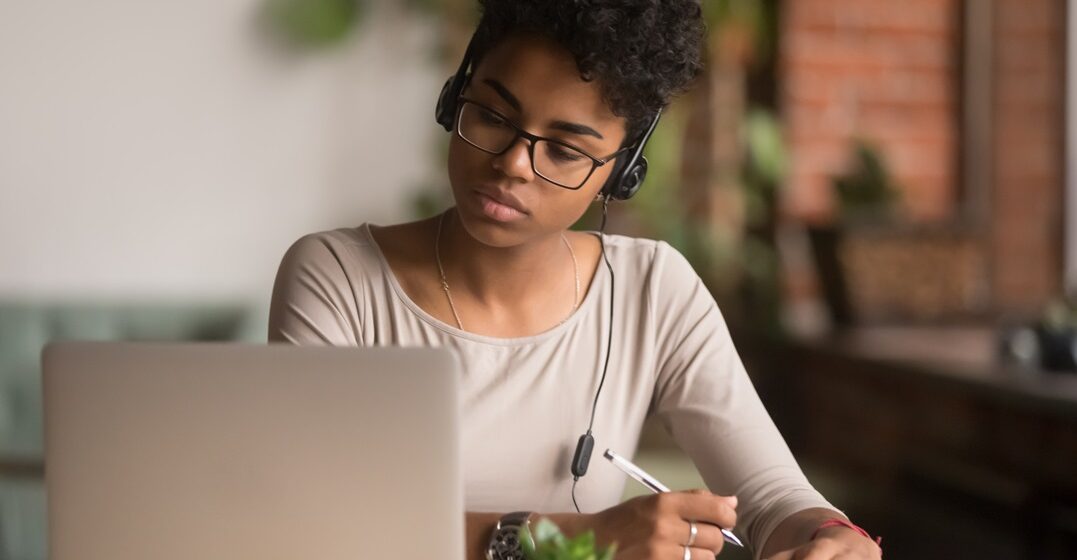 Focused,Mixed,Race,Woman,Wearing,Headphones,Watching,Webinar,Write,Notes
