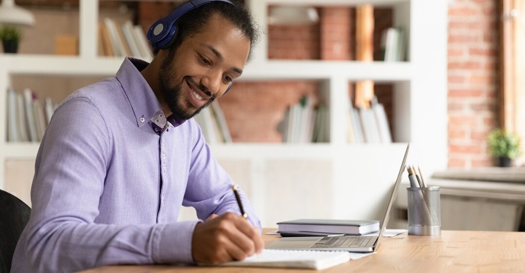 Young African American man on his laptop checking the best online English courses and taking notes