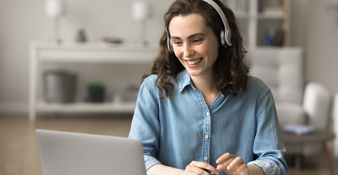 Junge Frau mit einem Headset sitzt an ihrem Laptop und lernt eine Fremdsprache