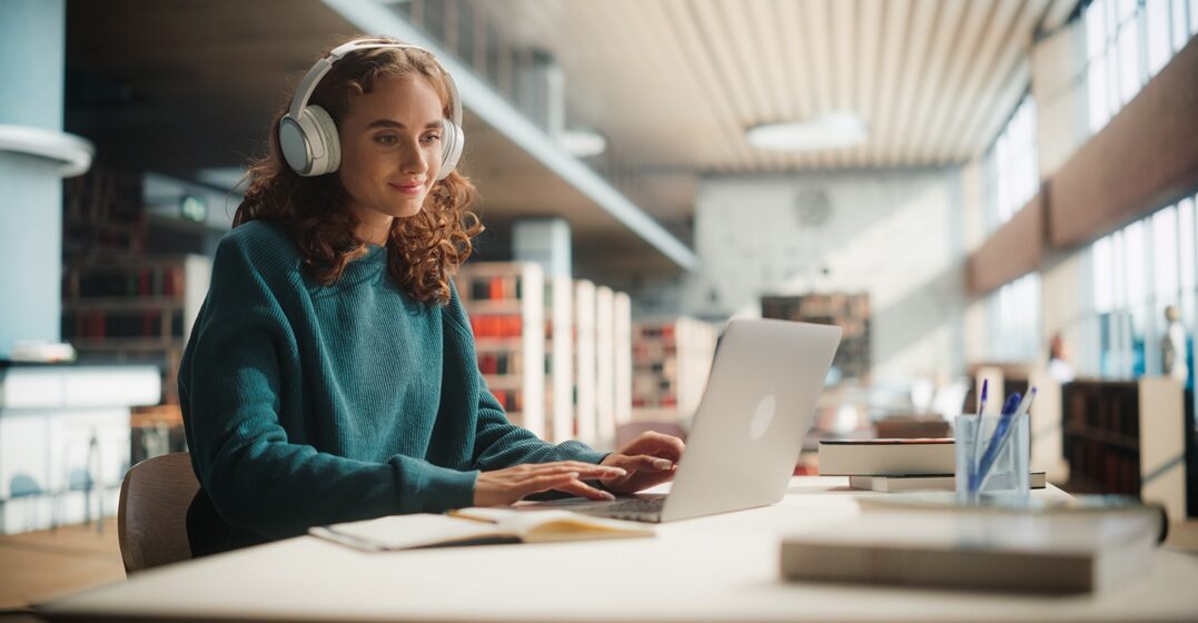young girl sitting at her desk, listening to the volere conjugation on her headphones