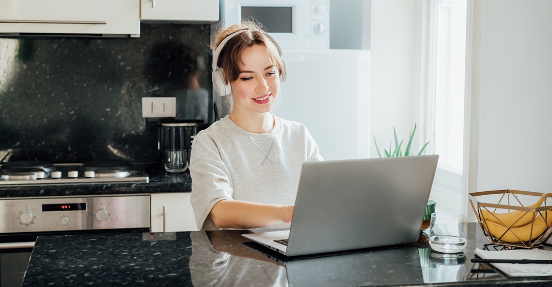 Junge Frau sitzt am Laptop in ihrer Küche und lernt Deutsch mit einem der besten Online-Deutschkurse