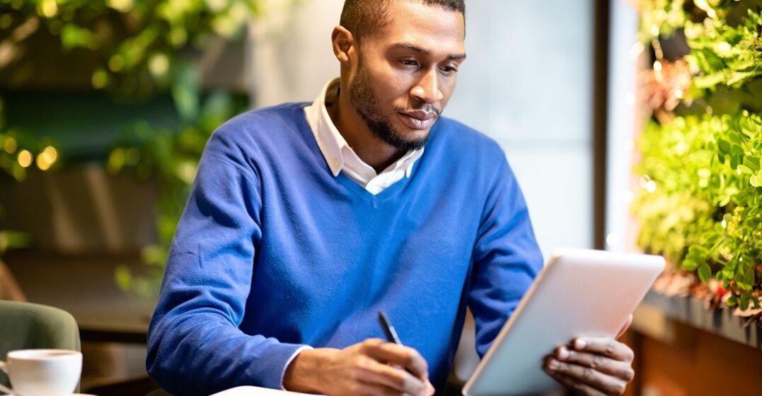 black man at his desk, holding a tablet and noting down the Italian alphabet