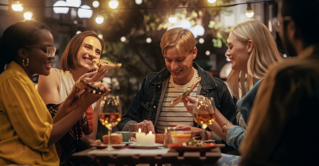 group of friends around a table eating some pizza, having fun and practicing Italian conversation
