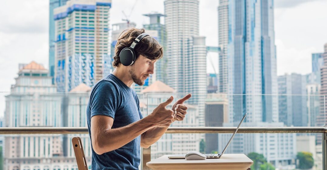 young man sitting at a table on his laptop woth a background view on the city and learning possessive adjectives in Italian