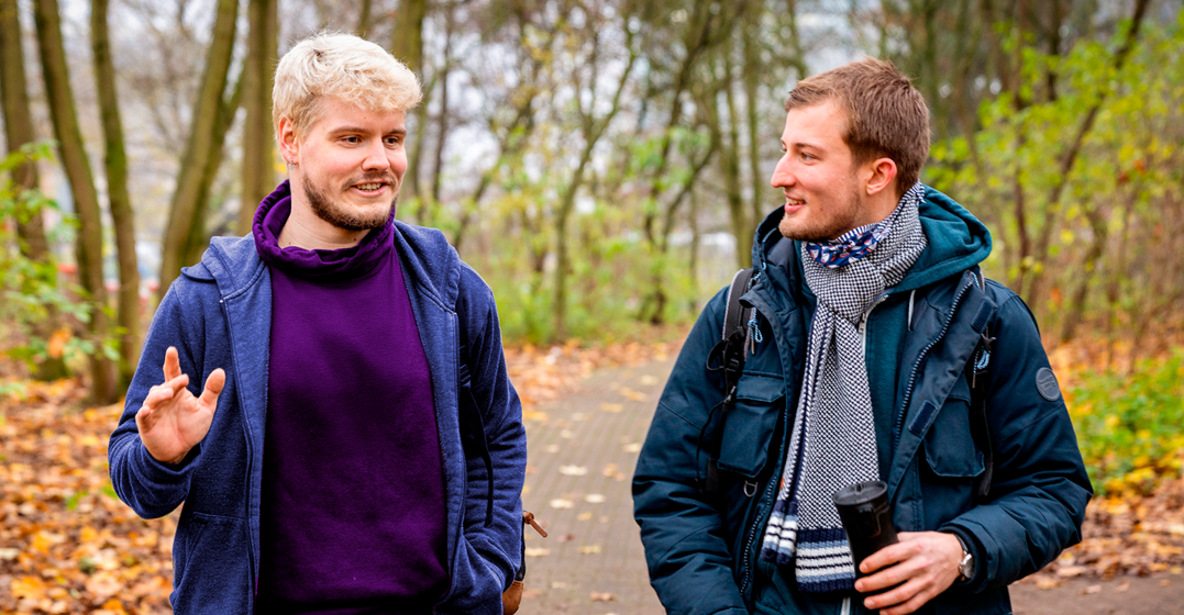 Two young men walking through a park talking about German nouns
