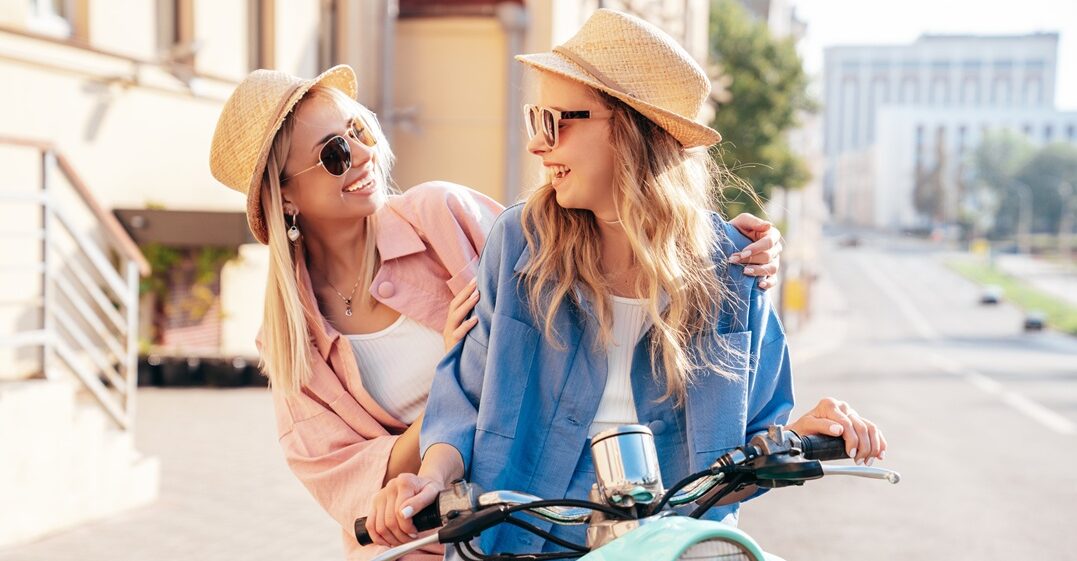 two girls on a vespa expressing their emotions in italian, smiling to each other