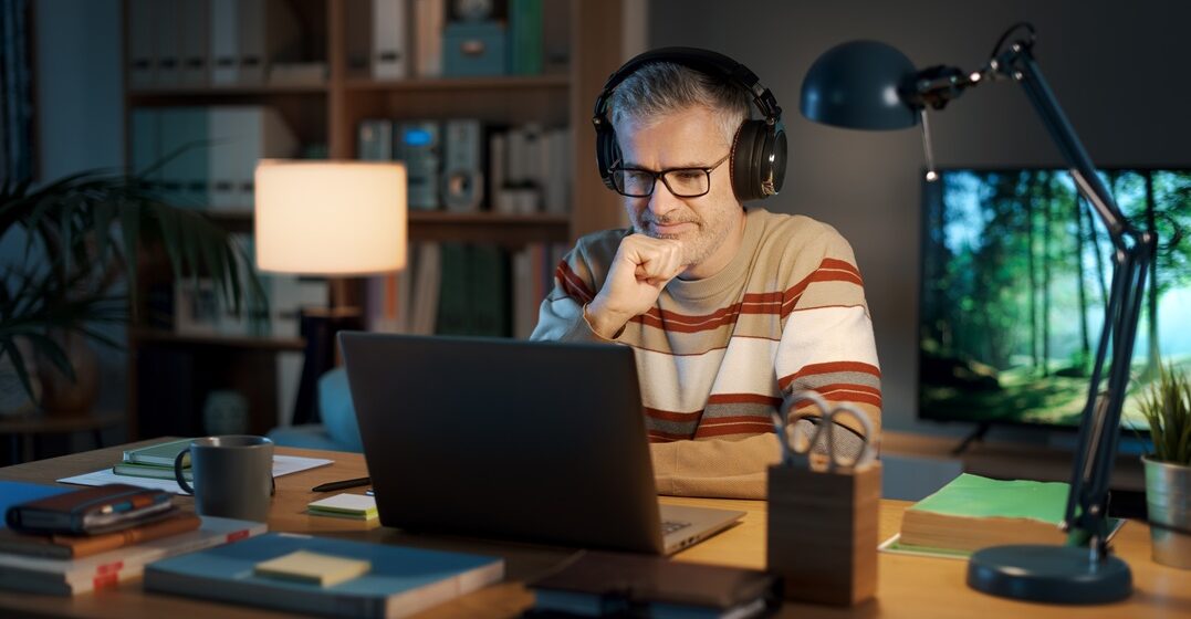 middle agned man sitting at his laptop with ehadphones on learning about German irregular verbs with Lingoda