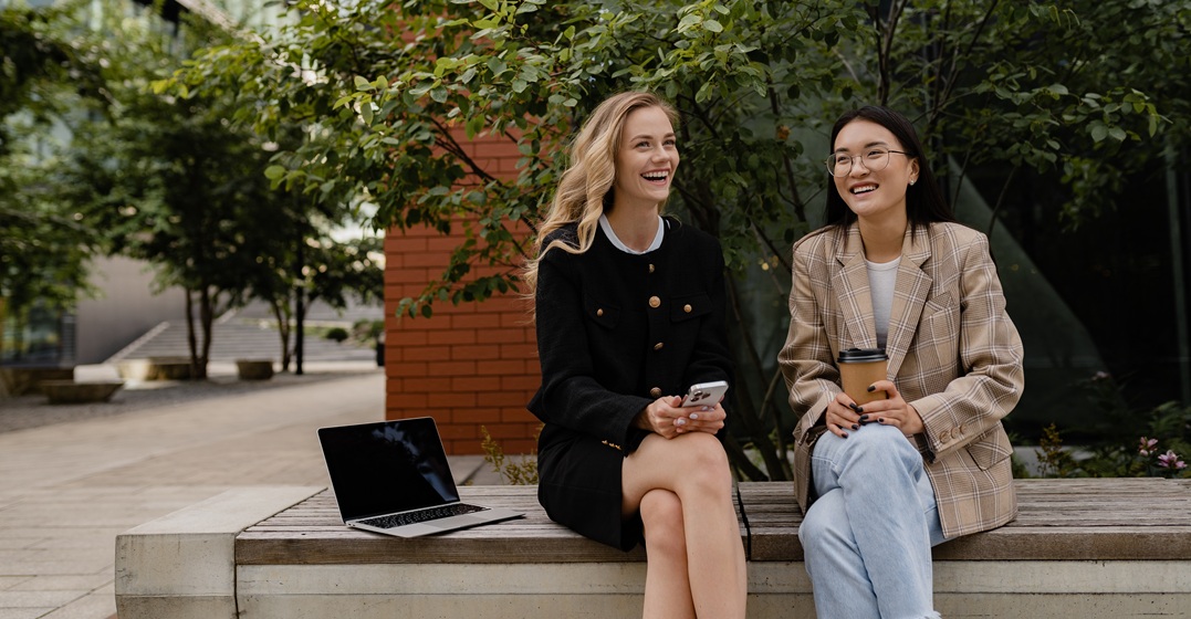 Zwei Frauen sitzen auf einer Bank mit einem Laptop und üben die deutschen Relativpronomen