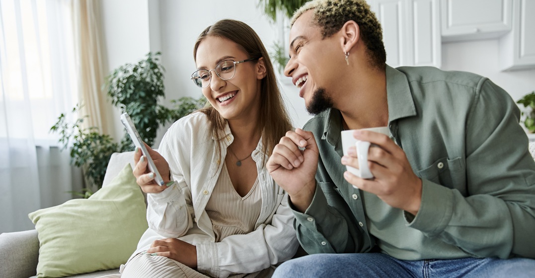 Zwei Freunde sitzen zusammen auf dem Sofa und lesen deutsche Zungebrecher auf ihrem Handy vor