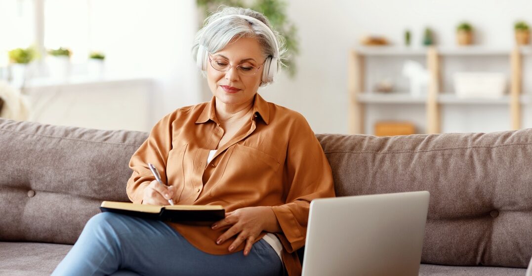 elderly caucasian woman sitting on the sofa and making notes on the haben conjugation in German