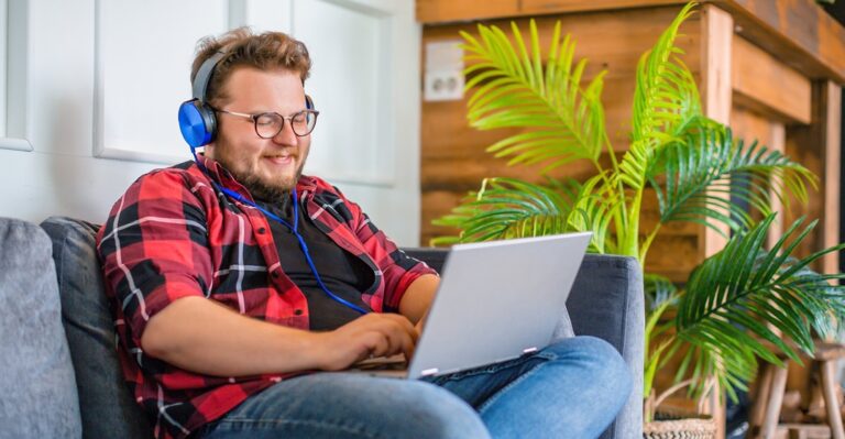 young hipster man sitting on a sofa and learning online with Lingoda the present progressive in English