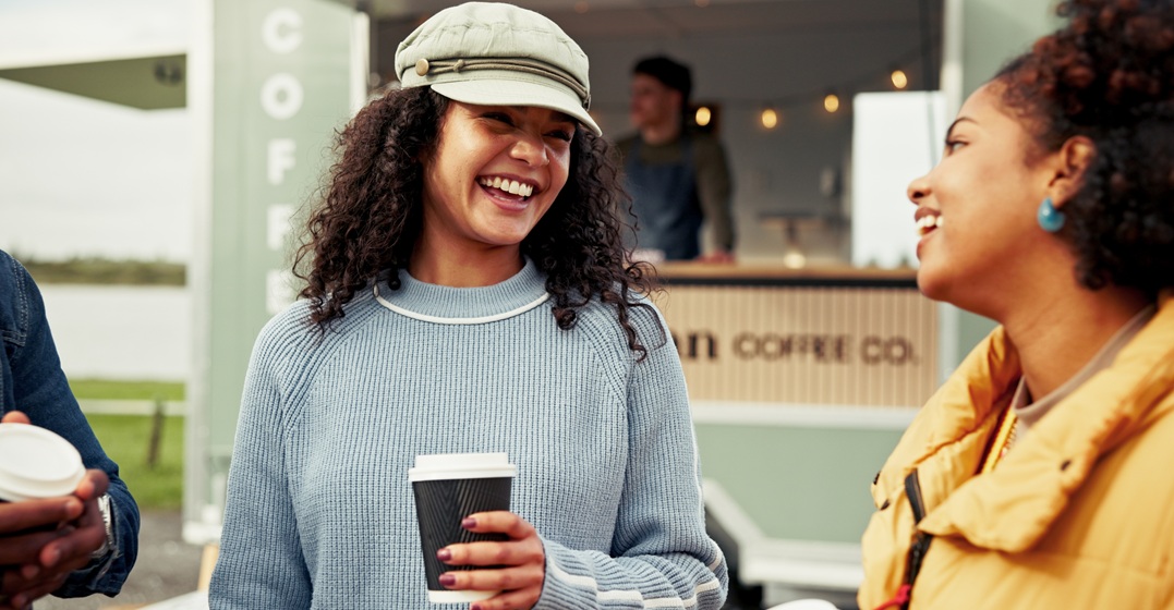 Zwei junge Frauen mit einem Kaffeebecher üben die Relativsätze auf Deutsch