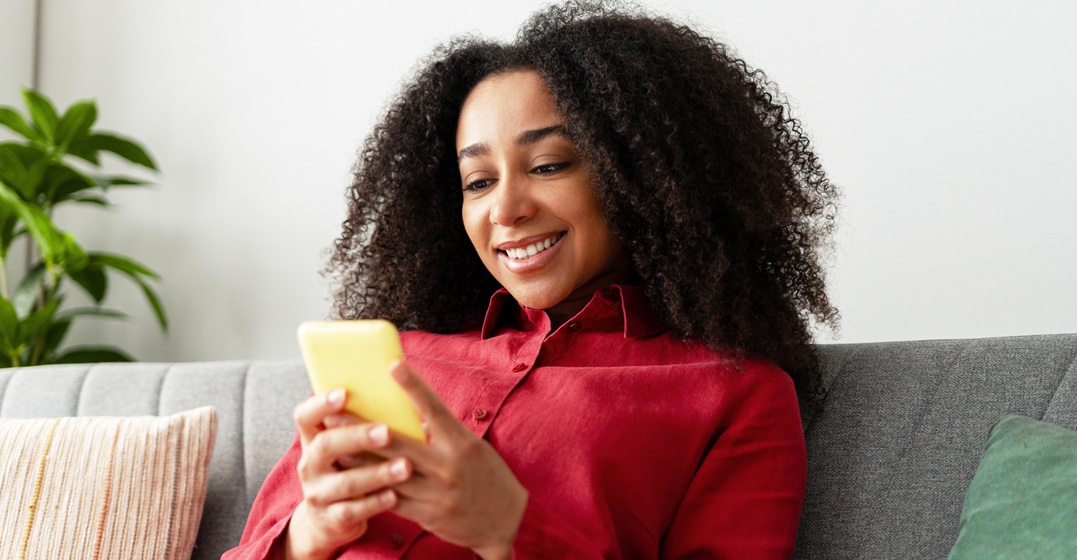 Fröhliche Afroamerikanerin sitzt am Handy und lernt das Gerundiv im Deutschen