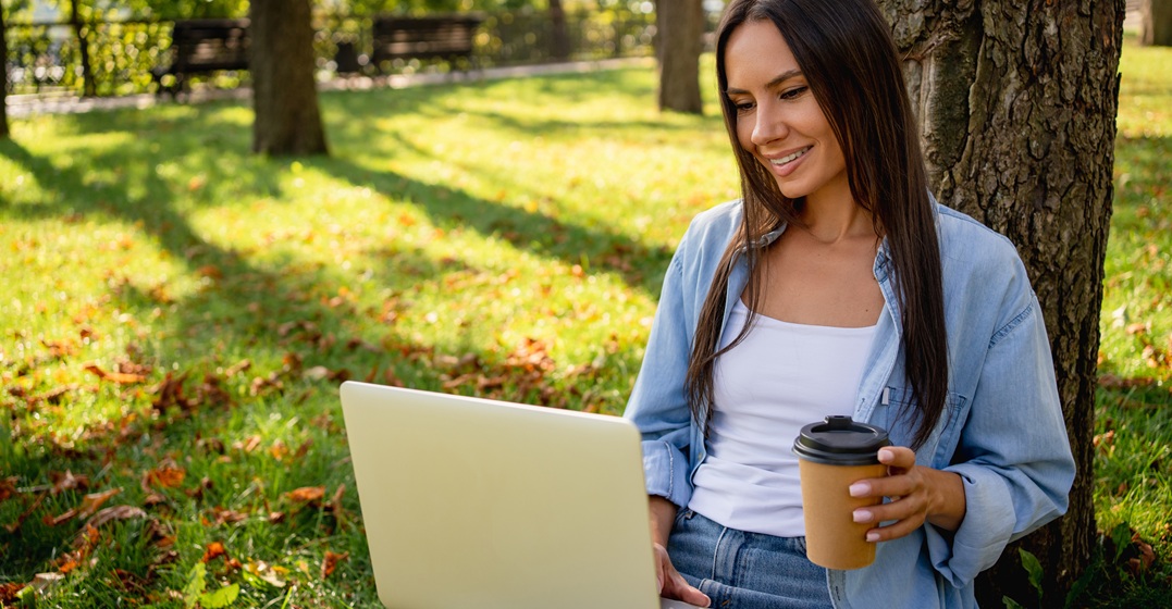 EIne junge Frau sitzt mit einem Kaffee am Laptop und übt die Adjektive mit -ig