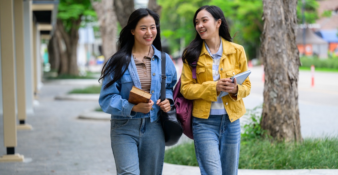 Zwei asiatische Studentinnen tragen Bücher im Laufen und unterhalten sich über Reflexive Verben mit Präpositionen