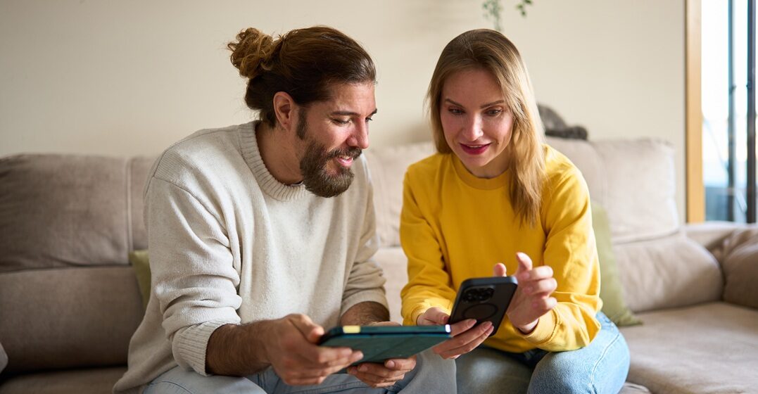 A couple of freinds, sitting on the sofa and checking to compare lingoda vs rosetta stone from their phone and tablet
