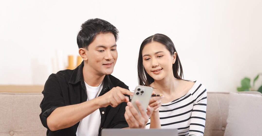 A mand and a woman of Asian origin sitting on the sofa and comparing lingoda vs goethe to learn German