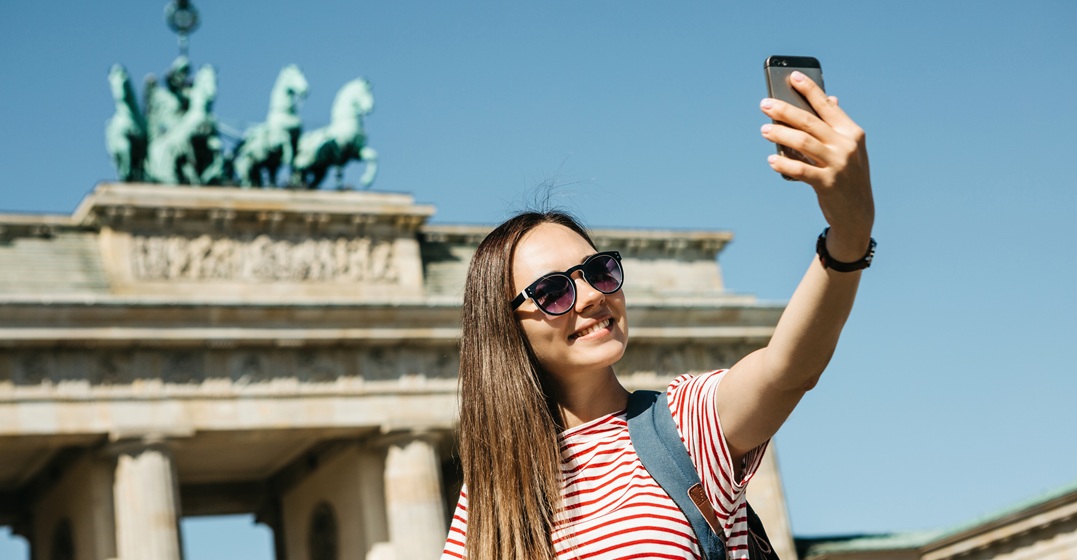 Smiling woman taking a selfie in front of Brandenburg gate